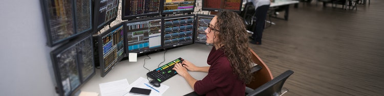 A woman sitting across multiple desktop monitors and typing on a keyboard