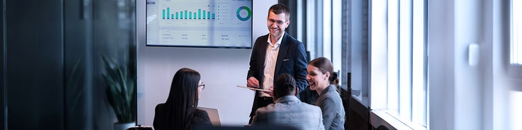 Professionals meeting in office reviewing dashboard charts on wall screen