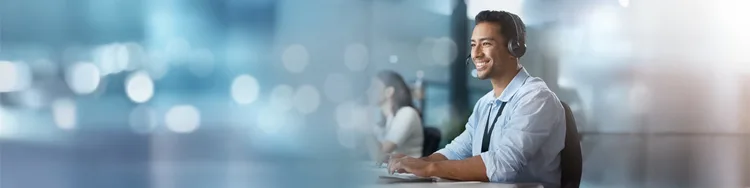 A man seated at a desk, focused on his laptop, with a notepad and pen beside him.