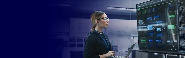 An engineering professional working on a laptop while viewing data on a transparent screen