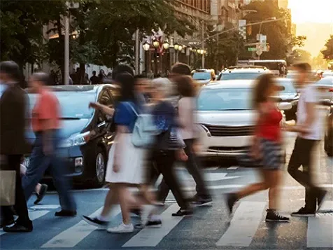 Pedestrians crossing a busy urban intersection during rush hour.