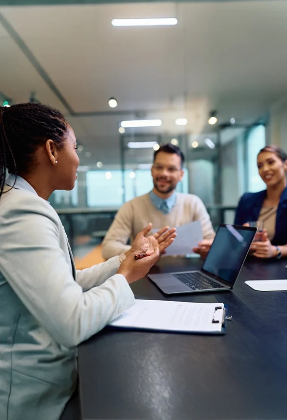 Three professionals meeting around a conference table with a laptop and documents.