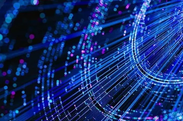 Abstract digital illustration of glowing blue and pink light streaks and particles forming flowing lines against a dark background, evoking data or network connectivity.