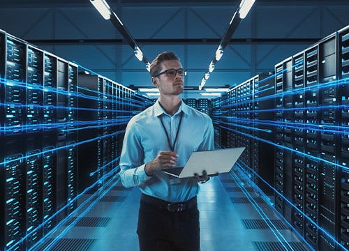 An engineer taking notes on a laptop inside a server room