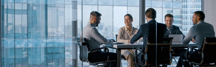 Business professionals collaborating in modern glass-walled office meeting room