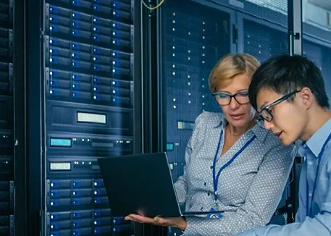 A female engineering showing a laptop screen to a colleague while standing next to servers