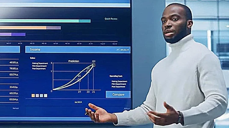 A person giving a presentation next to a digital screen