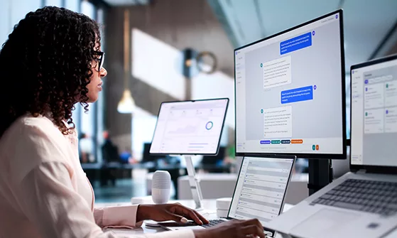A lady sitting on a chair and working on multiple computer monitors in front of her