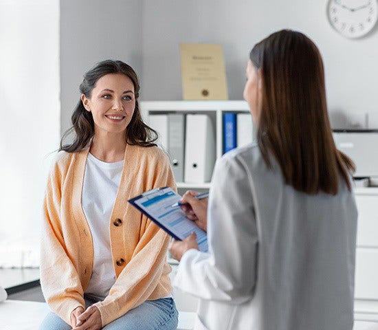 A woman seated in a chair talks to her doctor about insurance options during a medical appointment